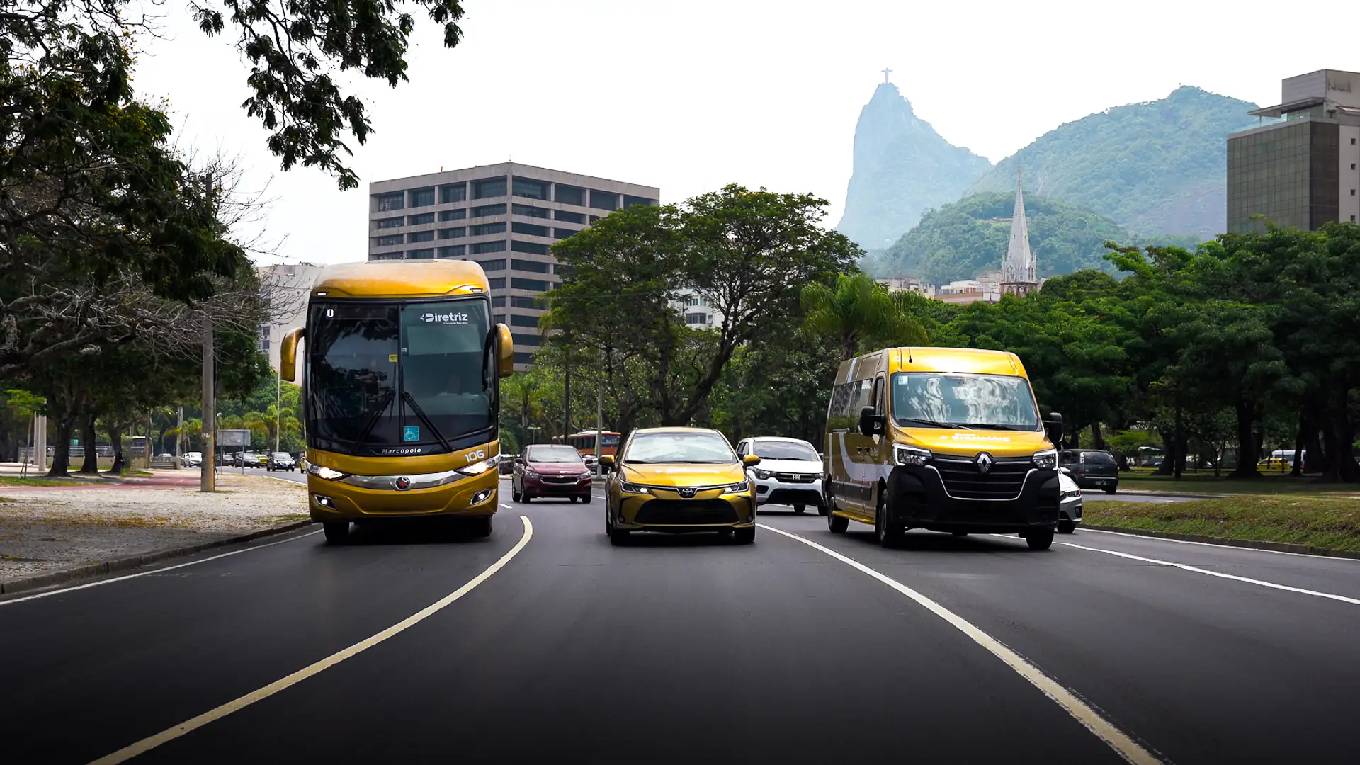 Ônibus, van e carro executivo da Braslectra em avenida do Rio com o Cristo Redentor ao fundo