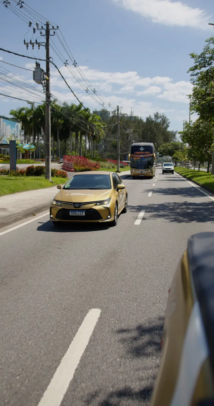 Toyota Corolla da frota executiva e ônibus em avenida arborizada